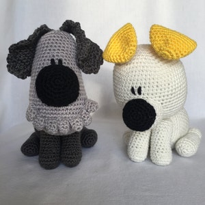 May include: Two crocheted stuffed dogs, one grey with black ears and nose, the other white with yellow ears and a black nose.