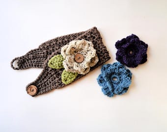 May include: A dark brown crocheted headband featuring a cream-coloured crocheted flower with two light green leaves and a wooden button centre. The headband has a wooden button closure. Two additional crocheted flowers in dark purple and blue are included.