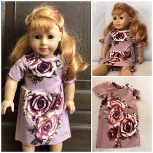 May include: A purple and pink floral dress with short sleeves for an 18-inch doll. The dress has a pocket on the front and a rose pattern.