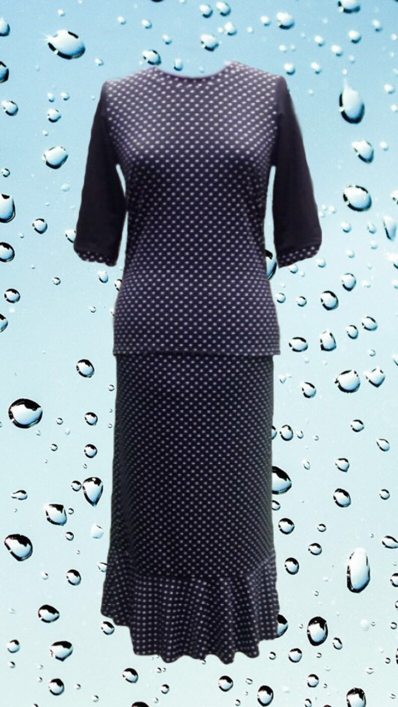 May include: A two-piece outfit consisting of a dark navy blue top and a matching skirt, both featuring a white polka dot pattern. The top has three-quarter length sleeves, and the skirt is a long, straight cut with a ruffled hem at the bottom.