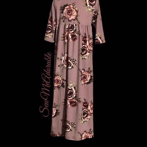 May include: A long-sleeved mauve dress with a floral print featuring pink and burgundy roses. The dress has a gathered waist and a relaxed fit.