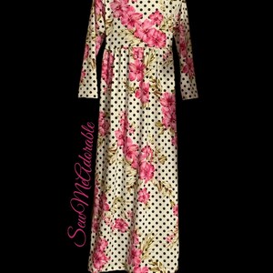 May include: A white long-sleeved dress with a floral and polka dot pattern. The dress has a pink floral print on a white background with black polka dots. The dress has a gathered waist and long sleeves.