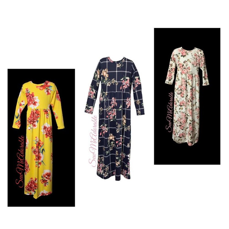May include: Three long-sleeved floral dresses in yellow, navy blue, and white. The dresses have a gathered waist and long sleeves. The text "Saw McAdorable" is printed on the side of each dress.
