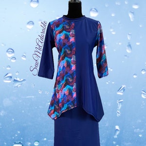 May include: A navy blue tunic with three-quarter sleeves and a high neckline, featuring an asymmetrical panel with a multi-colored abstract pattern in shades of blue, purple, and pink. The text SewMeAdorable is printed on the left side.
