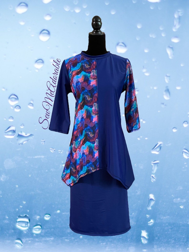 May include: A navy blue tunic with three-quarter sleeves and a high neckline, featuring an asymmetrical panel with a multi-colored abstract pattern in shades of blue, purple, and pink. The text SewMeAdorable is printed on the left side.