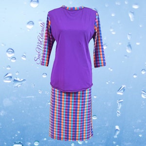 May include: A two-piece outfit consisting of a solid purple long-sleeve top and a matching skirt. The sleeves and skirt feature a vibrant plaid pattern in orange, blue, and purple. The text SewMeAdorable is printed on the left side of the top.