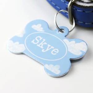 May include: Blue dog collar with a bone-shaped tag that says "Skye" in white lettering. The tag has a white cloud design.