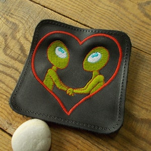 Op de afbeelding: Zwarte leren patch met een rood hart en twee groene aliens die elkaar de hand vasthouden in het hart. De aliens hebben blauwe ogen.