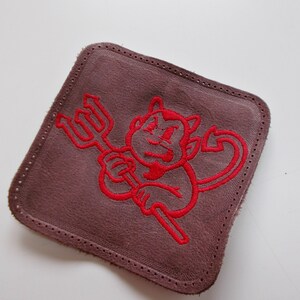 Peut inclure: Un patch en cuir marron avec un diable brodé en rouge tenant une fourche.
