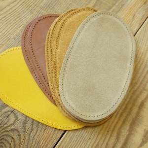 May include: Four oval-shaped leather patches in different colors: yellow, brown, tan, and beige. The patches have a stitched edge and are arranged in a semi-circle.