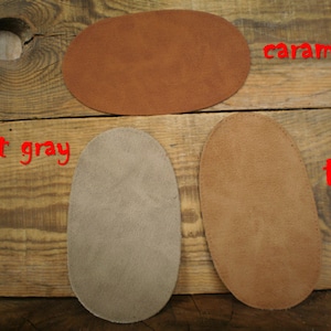 Könnte beinhalten: Drei ovale Lederstücke in den Farben Karamell, Hellgrau und Beige liegen auf einer rustikalen Holzoberfläche. Die Wörter "caramel", "light gray" und "tan" sind rot über jedem Stück geschrieben. Das Holz hat eine rustikale, gealterte Optik.