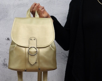 May include: A gold-colored faux leather backpack with a silver buckle and adjustable straps.