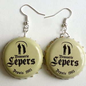 Puede incluir: Un par de pendientes hechos con tapas de botellas de cerveza. Cada tapa presenta un logotipo en blanco y negro para Brasserie Lepers, con el texto "Brasserie Lepers" y "Depuis 1905".