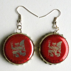 May include: A pair of red bottle cap earrings with a silver devil design and the text "DUYCK" and "GENUINE QUATRE SAISONS" on each cap.