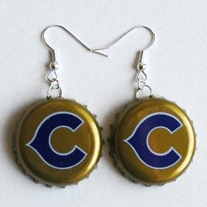 Puede incluir: Un par de pendientes hechos de tapas de botellas doradas con un logotipo "C" azul. Los pendientes tienen ganchos plateados.