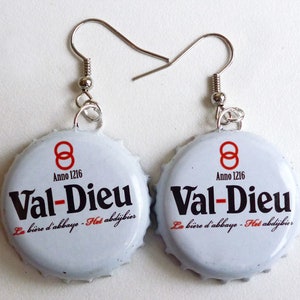 May include: A pair of earrings made from Val-Dieu beer bottle caps. The bottle caps are white with black text that reads "Val-Dieu" and "La bière d'abbaye - Het abdijbier". The bottle caps have a red 8 symbol and the text "Anno 1216".