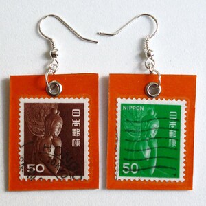 Puede incluir: Un par de pendientes con sellos postales japoneses vintage con fondo naranja. Los sellos representan a una mujer con un vestido tradicional japonés y el texto "NIPPON" y "50".