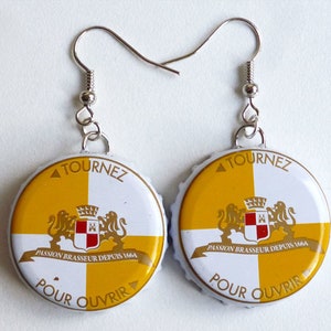 May include: A pair of handmade earrings featuring bottle caps with a yellow and white design. The caps have the text "TOURNEZ" and "POUR OUVRIR" printed on them, along with a crest and the text "PASSION BRASSEUR DEPUIS 1664".
