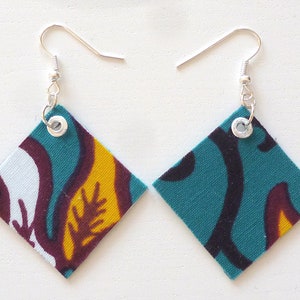 Puede incluir: Un par de pendientes en forma de diamante con un tejido estampado en azul verdoso, negro, blanco y amarillo. Los pendientes tienen ganchos plateados y ojales plateados.