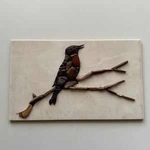 May include: A brown and black bird made of small stones is perched on a branch made of twigs. The bird is singing and has its beak open. The background is a light beige.