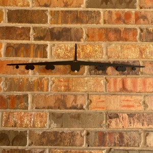 May include: A black metal silhouette of a B-2 Spirit bomber plane mounted on a brick wall.