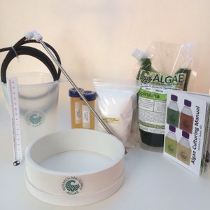 May include: An algae culturing kit with various components, including a white ring, a clear bucket with a ruler, and a bag labeled "Spirulina." The kit also includes a manual and several small containers.