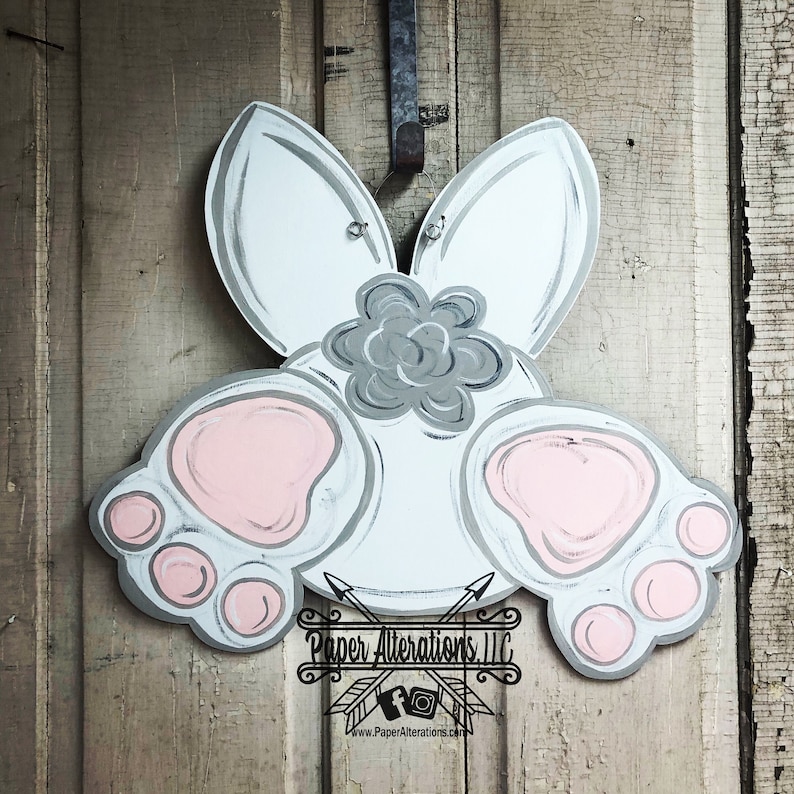 May include: White bunny rabbit door hanger with gray ears, a gray flower, and pink paw prints. The bunny is hanging on a wooden door. The text "Paper Alterations, LLC" is at the bottom of the image.