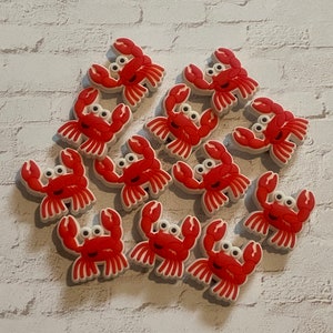 May include: A collection of 15 red and white plastic crab charms. The crabs have googly eyes and are arranged in a circle.