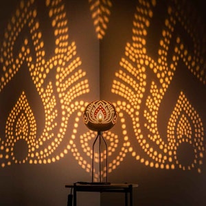 May include: A decorative lamp made from a carved coconut shell with a geometric pattern. The lamp casts a warm, golden light onto the wall, creating a beautiful shadow pattern.