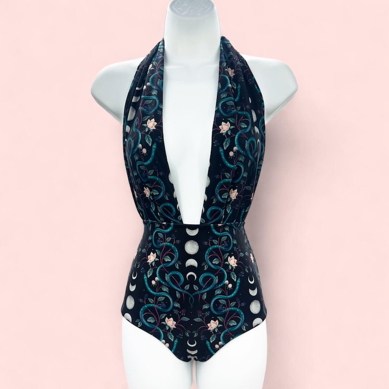 Witchy one-piece goth swimsuit with deep plunge neckline, featuring a celestial moon phase and serpent print on a black background.
