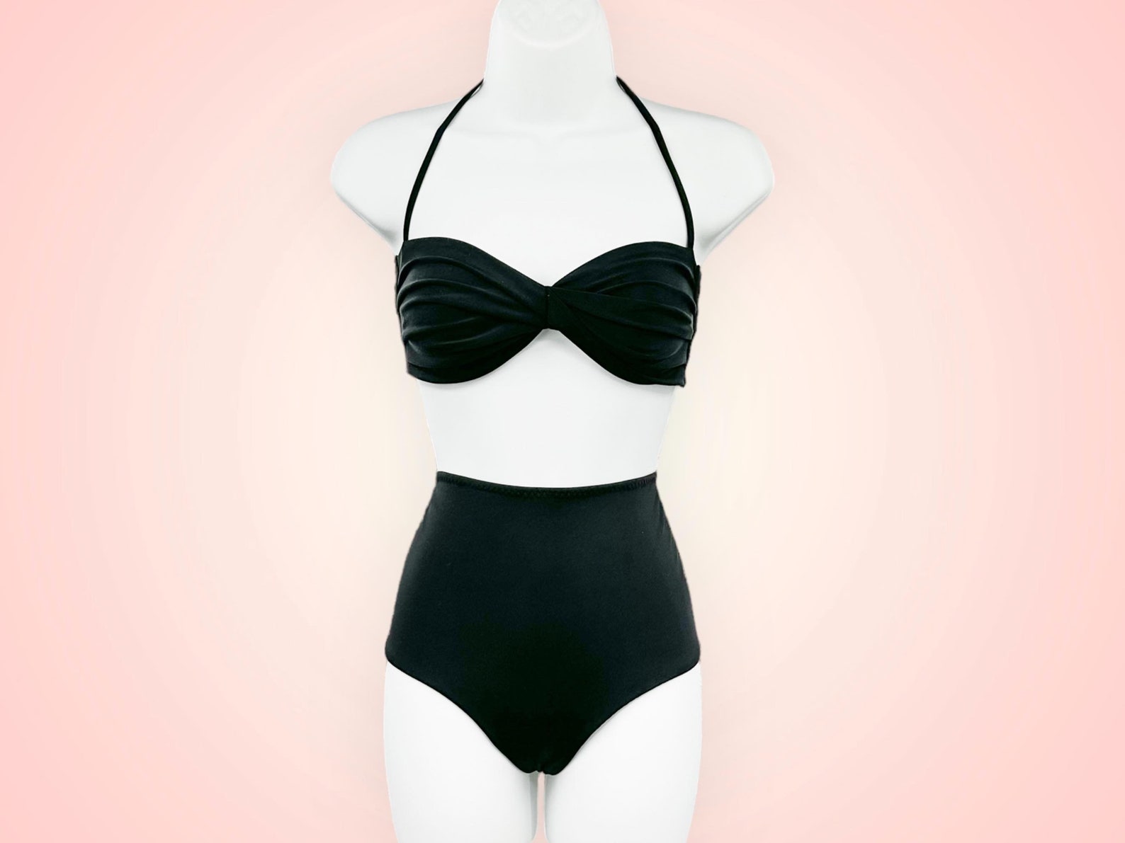 Black high-waisted bikini with a ruched bandeau-style top on a mannequin against a soft pink background.