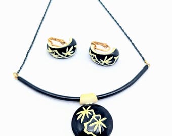 May include: A vintage jewelry set featuring a black necklace with a circular pendant and matching clip-on earrings. The pendant and earrings have a black background with a cream-colored leaf design. The necklace has a black chain.