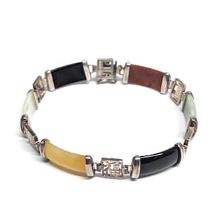 May include: A silver bracelet featuring alternating segments of black, brown, yellow, white, and green jade. The jade pieces are connected by silver links with a decorative square design. The bracelet is displayed against a white background.