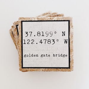May include: A set of four beige stone coasters with a white square tile on top. The tile has black text that reads "37.8199° N 122.4783° W golden gate bridge".