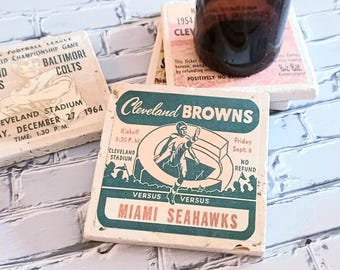 Könnte beinhalten: Quadratische Untersetzer aus Stein mit Vintage-Football-Ticket-Designs. Ein Untersetzer zeigt den Text Cleveland Browns gegen Miami Seahawks mit einer Spieler-Grafik. Ein anderer zeigt ein Ticket-Design für das Baltimore Colts Meisterschaftsspiel 1964.