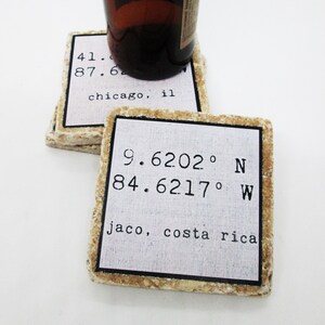 May include: Two square stone coasters with rough, textured edges. Each features a white center panel with a black border, displaying printed coordinates and location names. One reads 9.6202° N 84.6217° W jaco, costa rica, and the other shows Chicago, IL.