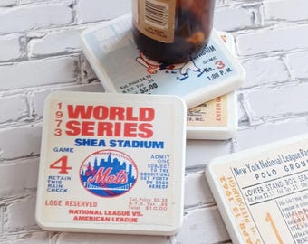 May include: Three square ceramic coasters featuring vintage baseball ticket designs. One coaster displays a 1973 World Series Shea Stadium ticket with the Mets logo, another shows a 1969 ticket, and the third features a 1962 Polo Grounds ticket.