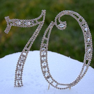 May include: Silver cake topper shaped like the number 70, decorated with clear rhinestones.