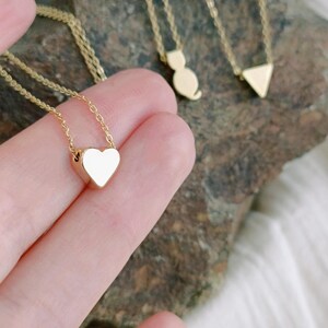 Puede incluir: Tres collares de oro con diferentes colgantes. El primer collar tiene un colgante en forma de corazón, el segundo un colgante en forma de gato y el tercero un colgante en forma de triángulo.