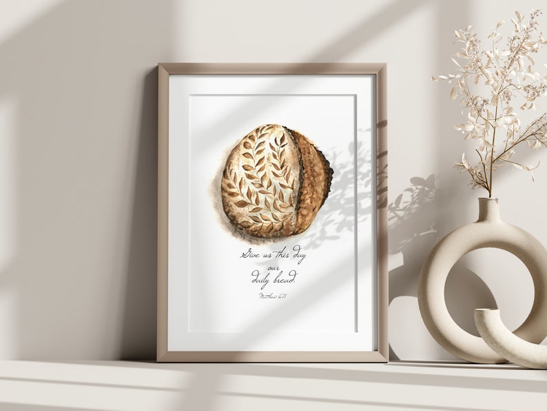 May include: A framed print with a watercolor illustration of a loaf of bread with the text "Give us this day our daily bread" and the scripture reference "Matthew 6:11".