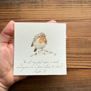 May include: Watercolor painting of a robin perched on a rock with the text "He set my feet upon a rock, and gave me a firm place to stand. Psalm 40"