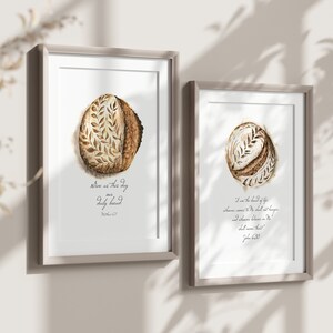 May include: Two framed prints with watercolor illustrations of sourdough bread. The first print features a loaf of bread with the text "Give us this day our daily bread" and the second print features a loaf of bread with the text "I am the bread of life, whoever comes to me shall not hunger and whoever believes in me shall never thirst."