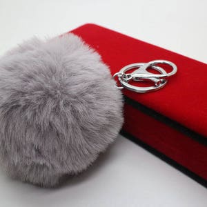 May include: A gray fluffy pom-pom keychain with a silver metal ring and a red velvet box.