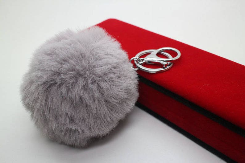 May include: A gray fluffy pom-pom keychain with a silver metal ring and a red velvet box.