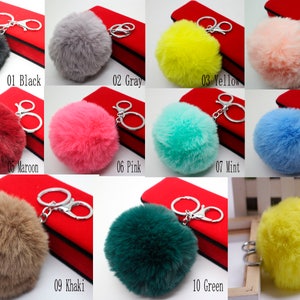 May include: Ten different colors of fluffy pom pom keychains. The keychains are attached to silver key rings. The colors are black, gray, yellow, peach, maroon, pink, mint, blue, khaki, and green.