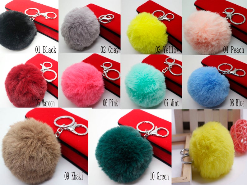 May include: Ten different colors of fluffy pom pom keychains. The keychains are attached to silver key rings. The colors are black, gray, yellow, peach, maroon, pink, mint, blue, khaki, and green.
