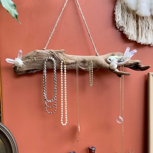 May include: A driftwood jewelry holder with a rope hanger, featuring crystal accents and seashells.  The holder is decorated with several necklaces and a crystal pendant.