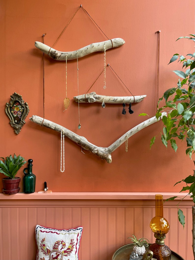 Puede incluir: Un organizador de joyas de madera flotante con tres ramas colgadas de la pared. Las ramas est&aacute;n decoradas con collares, pendientes y otras joyas. La pared est&aacute; pintada de un color naranja c&aacute;lido.