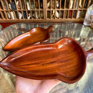 Op de afbeelding: Twee houten blaadjesvormige serveerschalen gemaakt van donkerbruin hout. De schalen zijn licht gebogen en hebben aan één kant een handvat.