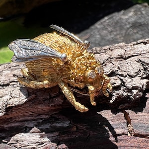 Puede incluir: Un broche de abeja de oro y plata con detalles de diamantes. La abeja está detallada con alas texturizadas y un cuerpo peludo.